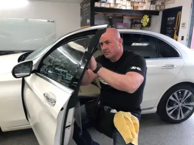 Mike applying window tint to a white car inside an auto sho